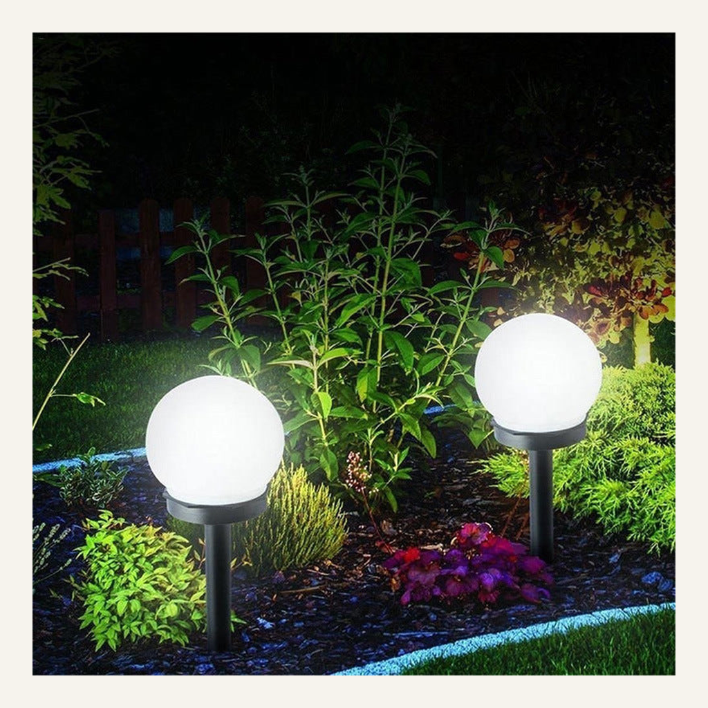 White solar globe garden lights illuminated in a planted bed